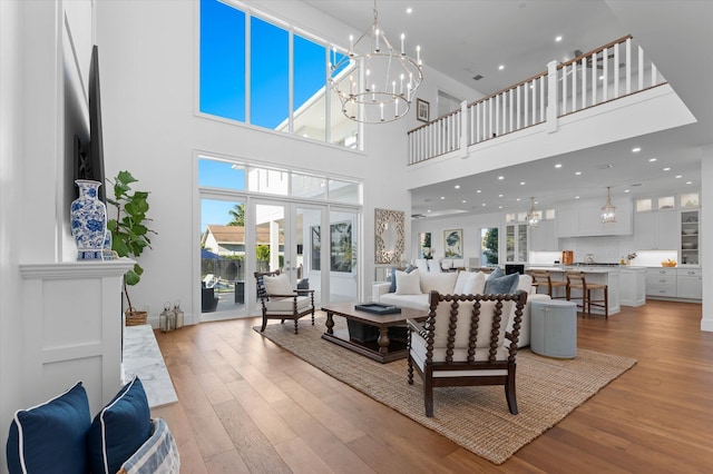 living room with a wealth of natural light, light wood-style flooring, a notable chandelier, and french doors