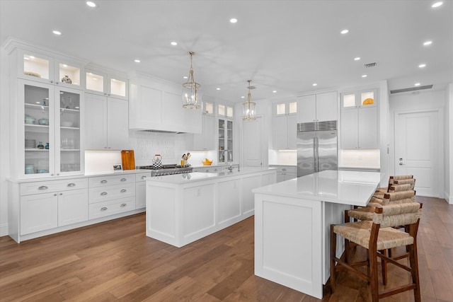 kitchen with light countertops, a large island, dark wood finished floors, and stainless steel built in fridge