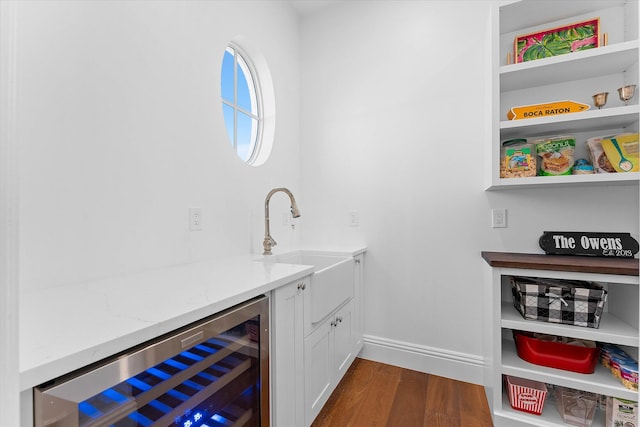 bar featuring dark wood-style floors, beverage cooler, a sink, and baseboards