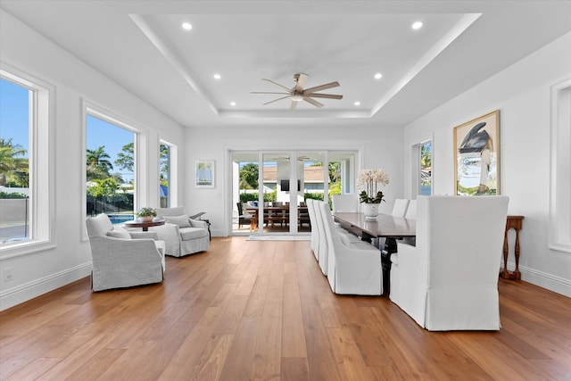 dining room featuring light wood-style floors, recessed lighting, a raised ceiling, and baseboards