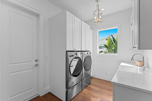 laundry area featuring cabinet space, light wood finished floors, washing machine and clothes dryer, an inviting chandelier, and a sink