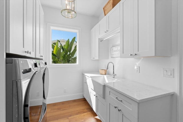 laundry room with cabinet space, light wood-style floors, washing machine and dryer, a sink, and baseboards