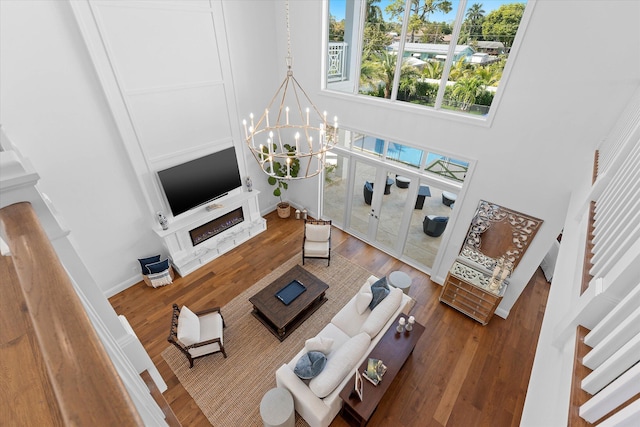 living room featuring a notable chandelier, a high ceiling, wood finished floors, baseboards, and stairs