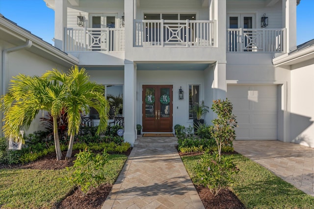 entrance to property with a garage, french doors, a balcony, and stucco siding