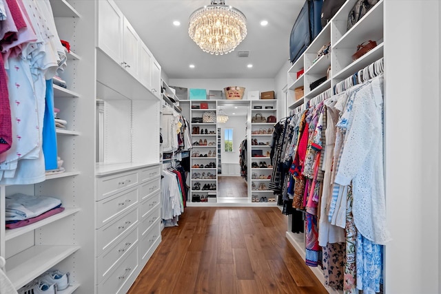 spacious closet with dark wood-style floors and an inviting chandelier