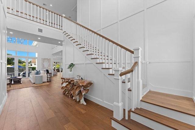 staircase with recessed lighting, visible vents, a decorative wall, a high ceiling, and hardwood / wood-style floors