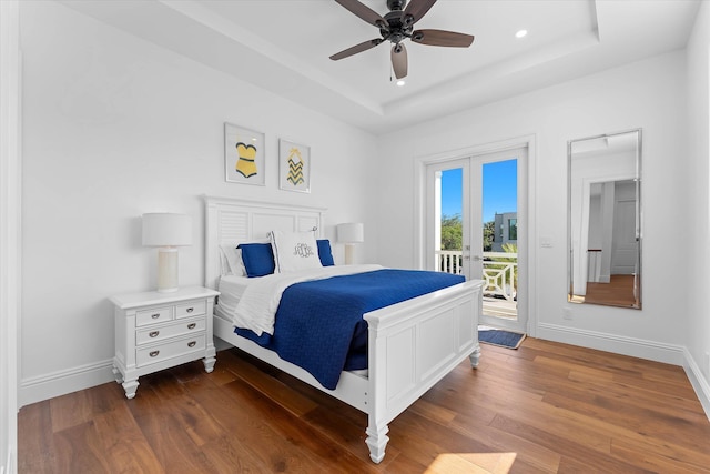 bedroom featuring access to outside, a raised ceiling, baseboards, and wood finished floors