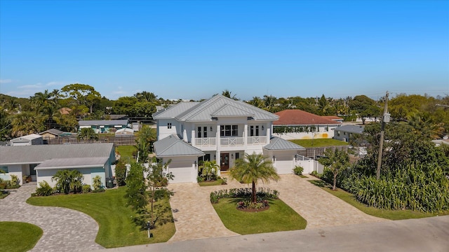 view of front of house with metal roof, a balcony, decorative driveway, a front lawn, and a standing seam roof