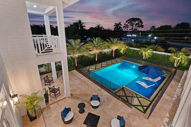 pool at dusk featuring a patio and fence