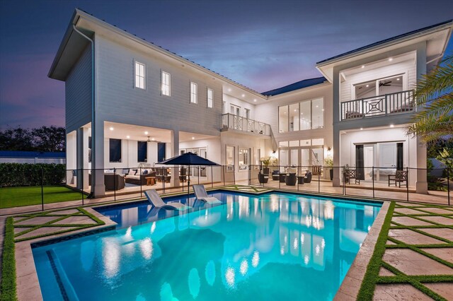 back of property at dusk featuring a balcony, fence, a fenced in pool, and a patio