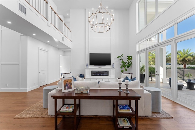 living area featuring a glass covered fireplace, visible vents, a notable chandelier, and wood finished floors