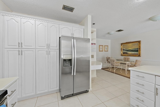 kitchen with light countertops, white cabinets, light tile patterned floors, and stainless steel fridge