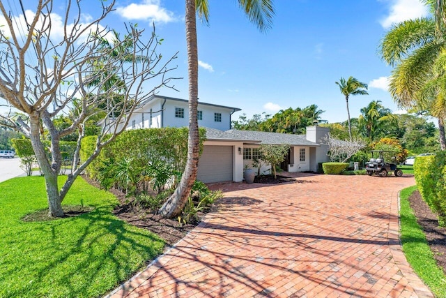 view of front of property featuring a chimney, stucco siding, a front lawn, a garage, and decorative driveway