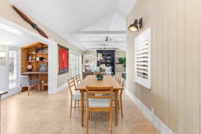 dining room featuring vaulted ceiling with beams, wood walls, and a ceiling fan