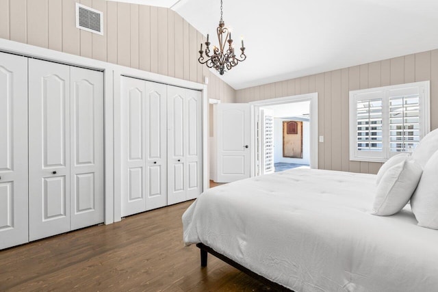 bedroom with two closets, lofted ceiling, visible vents, wood finished floors, and a chandelier