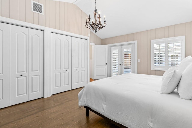 bedroom featuring multiple closets, lofted ceiling, visible vents, wood finished floors, and access to outside