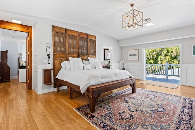 bedroom featuring lofted ceiling, a notable chandelier, light wood-style floors, access to exterior, and wainscoting