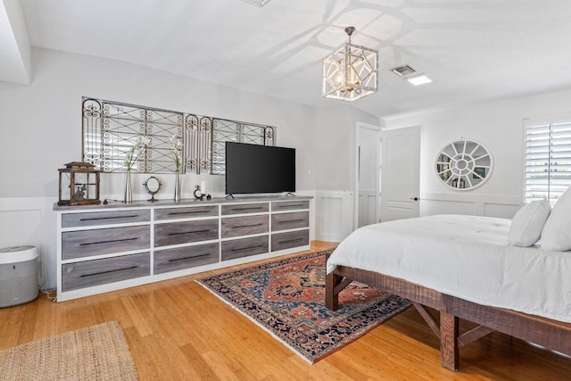 bedroom with a decorative wall, a notable chandelier, wood finished floors, visible vents, and wainscoting