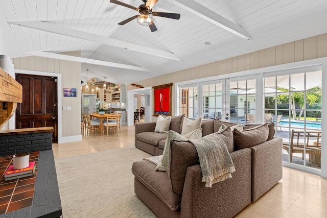 living area with vaulted ceiling with beams, light tile patterned flooring, wood walls, a ceiling fan, and french doors