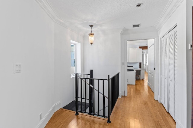 hallway with visible vents, light wood-style flooring, an upstairs landing, and crown molding