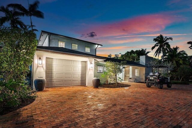 traditional-style house with a garage, decorative driveway, and stucco siding