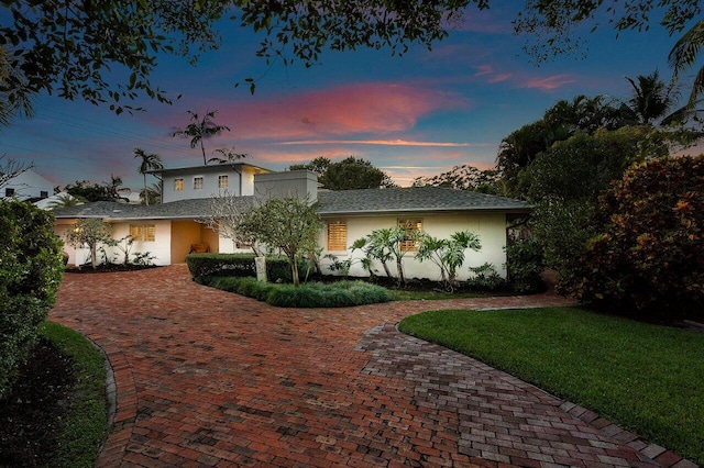 view of front of property featuring decorative driveway, a lawn, and stucco siding