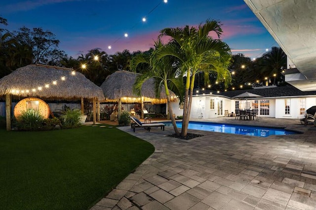 pool at dusk with an outdoor pool, a patio area, and a lawn