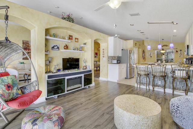 living room with light wood finished floors, visible vents, arched walkways, ceiling fan, and built in shelves