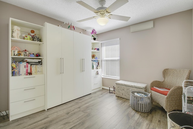 sitting room featuring a ceiling fan, light wood-style flooring, a textured ceiling, and a wall mounted AC