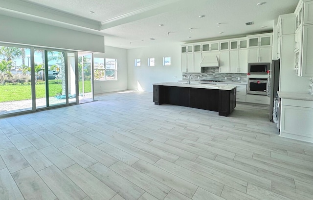 kitchen with custom exhaust hood, visible vents, backsplash, appliances with stainless steel finishes, and open floor plan