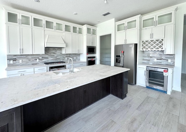 kitchen with white cabinets, wine cooler, custom exhaust hood, stainless steel appliances, and a sink