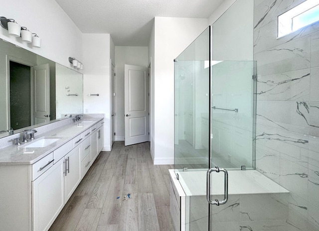 bathroom with double vanity, a sink, a shower stall, wood finished floors, and baseboards