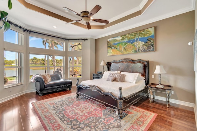 bedroom with baseboards, a raised ceiling, crown molding, and wood finished floors