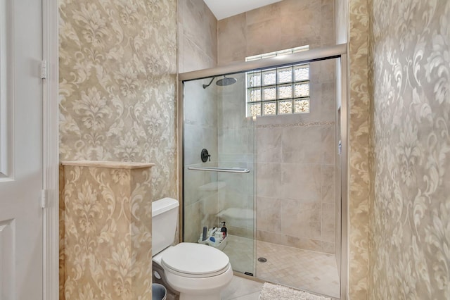 bathroom featuring toilet, wallpapered walls, and a shower stall