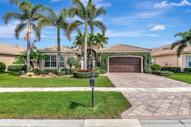 mediterranean / spanish-style home with decorative driveway, stucco siding, a garage, a tiled roof, and a front lawn