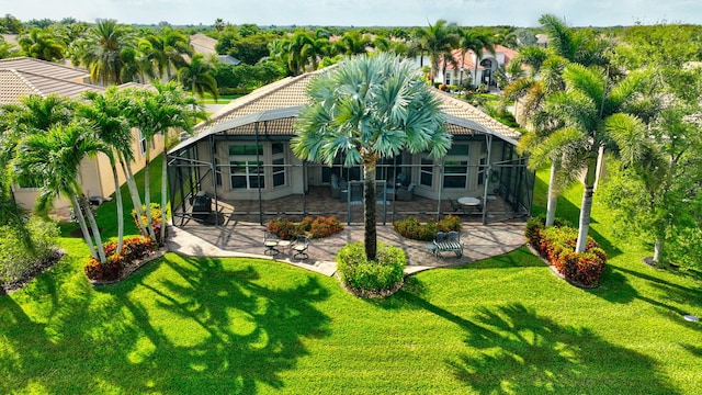 rear view of property featuring a tile roof, glass enclosure, a patio area, and a lawn