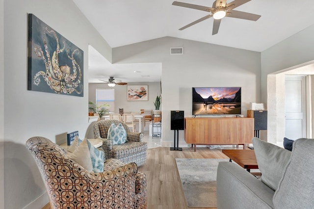 living room with lofted ceiling, light wood-style flooring, visible vents, baseboards, and a ceiling fan