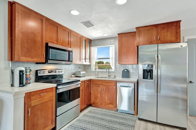 kitchen with brown cabinets, appliances with stainless steel finishes, light countertops, and a sink