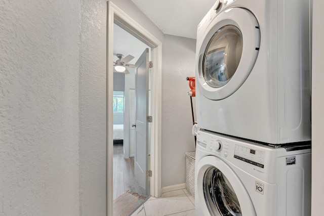 laundry area featuring a textured wall, marble finish floor, stacked washer / dryer, and baseboards