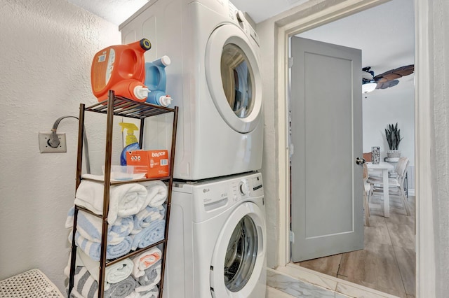 clothes washing area featuring laundry area, ceiling fan, stacked washer / dryer, and a textured wall