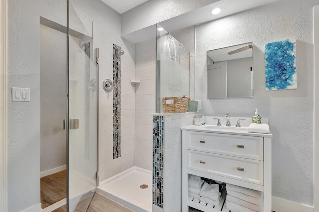 full bath with a shower stall, vanity, baseboards, and a textured wall