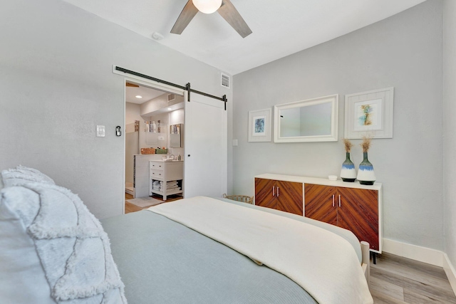 bedroom with visible vents, light wood-style flooring, a barn door, ceiling fan, and baseboards