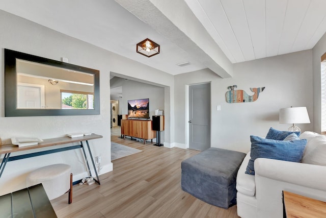 living room with light wood-type flooring, visible vents, baseboards, and beamed ceiling