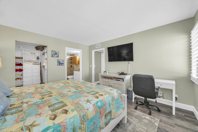 bedroom featuring visible vents, a spacious closet, ensuite bathroom, wood finished floors, and baseboards