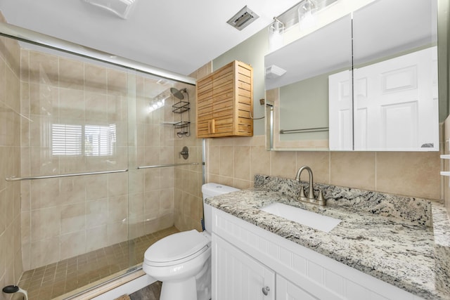 full bathroom featuring a stall shower, tile walls, toilet, and vanity