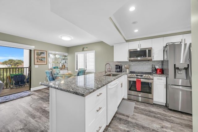 kitchen featuring appliances with stainless steel finishes, white cabinets, a sink, and a peninsula