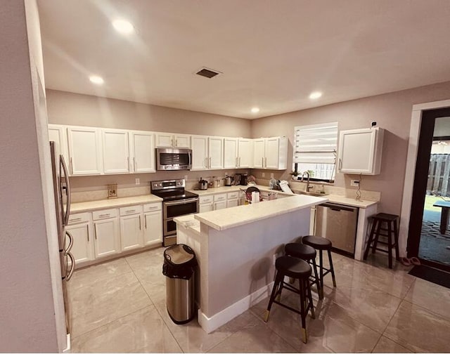 kitchen with appliances with stainless steel finishes, white cabinets, visible vents, and a kitchen bar