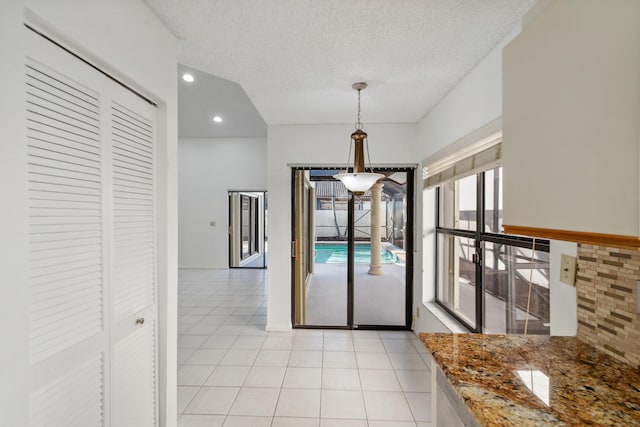 interior space featuring decorative light fixtures, light tile patterned floors, recessed lighting, a textured ceiling, and dark stone countertops