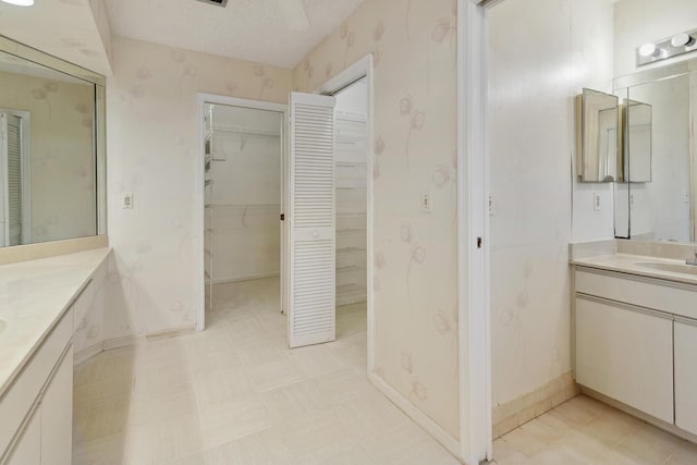 full bathroom with a textured ceiling, a sink, two vanities, and wallpapered walls