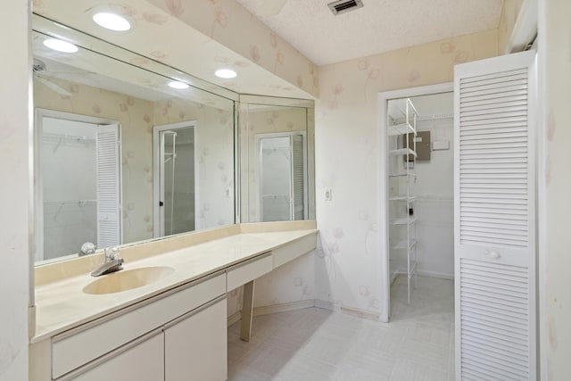 bathroom with visible vents, vanity, a textured ceiling, baseboards, and wallpapered walls